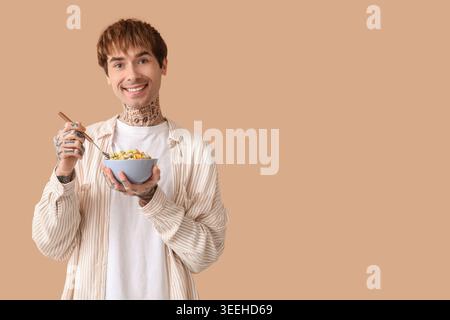 Mann hält Schüssel mit Müsliringen und Löffel auf beigefarbenem Hintergrund Stockfoto