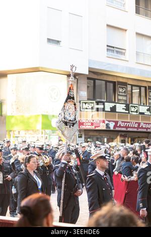 Almería, Spanien - 30. März 2026: Eine Marschkapelle und ein Prozessionsbanner bewegen sich während einer Karwoche durch eine überfüllte Straße Stockfoto