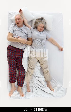 Älteres Paar, das auf dem Rücken in entspannten Positionen auf weißem Bett schläft. Stockfoto