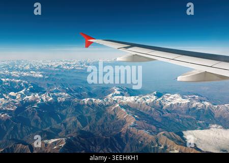 Eine Luftperspektive auf die schneebedeckten Alpen unter einem klaren blauen Himmel, aufgenommen von einem Flugzeugfenster während eines Fluges Stockfoto