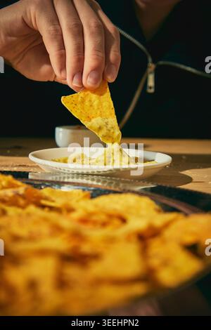 Tortilla-Chip in cremige Käsesauce auf Teller in appetitlicher Nahaufnahme getaucht Stockfoto