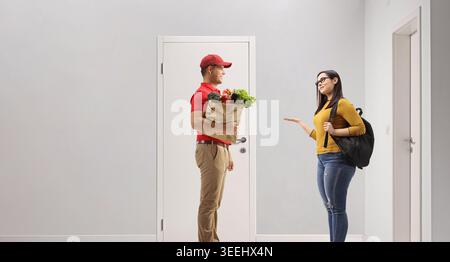 Ein Mann, der einer Studentin eine Tüte Lebensmittel vor einer Tür liefert Stockfoto