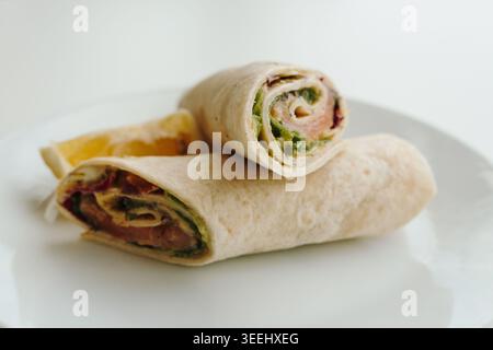 Lachs-Wrap-Rollen mit frischem Gemüse und Zitronenscheibe, serviert auf einem weißen Teller. Konzept für gesunden Fast Food, Café-Menü, ausgewogene Ernährung und Stockfoto