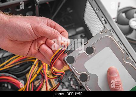 Ein Techniker verbindet während einer Computerbaugruppe ein SATA-Netzkabel mit einer Festplatte. Stockfoto
