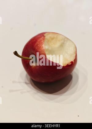 Nahaufnahme Roter Apfel Mit Sichtbarem Biss Auf Blasse Oberfläche, Glatter, Glänzender Haut, Studio-Beleuchtung Und Flacher Tiefe Stockfoto