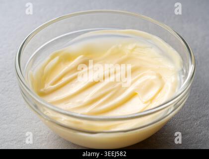 Cremige Mayonnaise mit Textur wirbelt in einer klaren Glasschale auf grauem Steinhintergrund Stockfoto