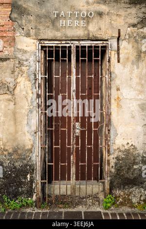 Eingang zu einem Tattoo-Salon über eine rustikale verwitterte dunkle Holztür, die in eine alte abblätternde Putzwand gesetzt ist, George Town, Penang, Malaysia Stockfoto