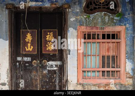 Nahaufnahme der architektonischen Fassade mit einer alten dunklen Holztür neben einem kontrastierenden rosafarbenen Fensterfenster, George Town, Penang, Malaysia Stockfoto