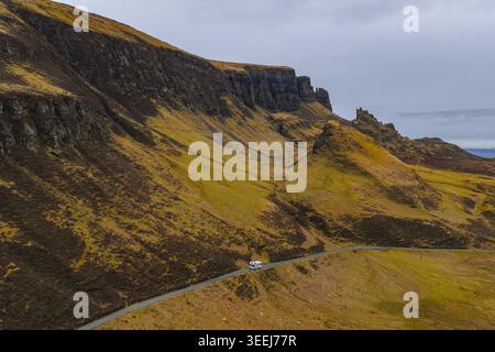 Aus der Vogelperspektive auf Quiraing mit einem weißen Wohnmobil, der auf einer kurvenreichen Straße durch die dramatische felsige Landschaft und die grünen Hänge der Isle of Skye, Scotl fährt Stockfoto