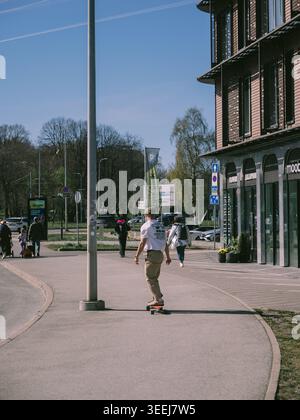 Junger Mann, der im Frühjahr auf einem sonnigen Bürgersteig an einem Backsteinhaus in Tallinn, Estland, vorbeifährt Stockfoto