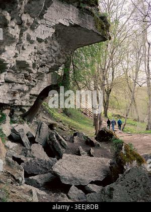 Besucher spazieren im Frühjahr auf einem Pfad unter Kalksteinklippen in der Nähe des Wasserfalls Jägala in Estland Stockfoto