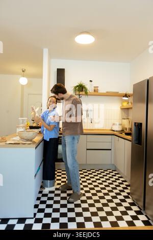 In einer hellen und stilvollen Küche lacht eine Koreanerin, während sie zusammen mit einem kaukasischen Mann kocht und fröhliche Momente schafft. Stockfoto