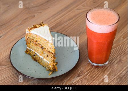 Karottenkuchenscheibe mit Frischkäse-Zuckerguss und frischem Fruchtsaft auf Holztisch Stockfoto