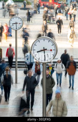 Pendler, die an Straßenuhren in Canary Wharf, London Docklands, vorbeilaufen. Stockfoto