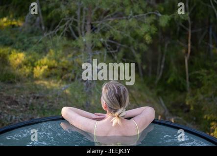 Frau, die sich im Whirlpool im Freien, umgeben von Wald Natur in skandinavischem Spa-Retreat entspannt Stockfoto