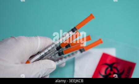 Handschuhe halten Orange Spritzen mit Biohazard Bag — medizinische Impfung und Biosicherheit Konzept Stockfoto