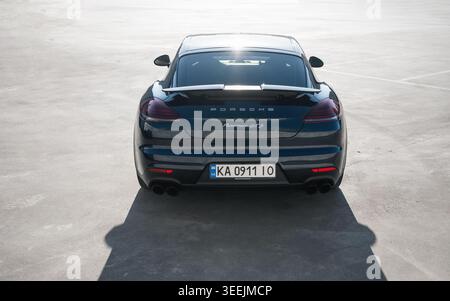 Dunkelblauer Porsche Panamera auf einem großen Parkplatz. Rückansicht des deutschen Grand Tourers, der auf einer riesigen Betonoberfläche geparkt ist, von hinten strahlende Sonne. Stockfoto