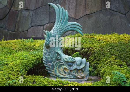 Tokio, Japan - 1. Oktober 2024, Nahaufnahme einer Bronzeskulptur der mythischen Kreatur Shachihoko, platziert zwischen Büschen in der Nähe einer Steinmauer auf dem Erdboden Stockfoto