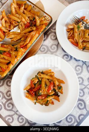Gebackene vegetarische Penne-Pasta mit Zucchini, Tomaten und Käse in einer Auflaufform und weißen Tellern. Hausgemachtes italienisches Lebensmittelfotografie-Konzept. Stockfoto