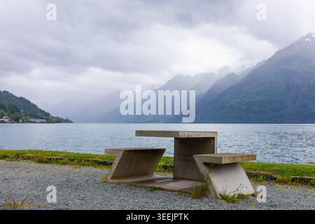 Ruhiger Zufluchtsort am Hardangerfjord mit Betontisch mit Blick auf ruhiges Wasser und überlagerten Bergen mit Regenwolken in Westnorwegen. Kontemplative Reise, S Stockfoto