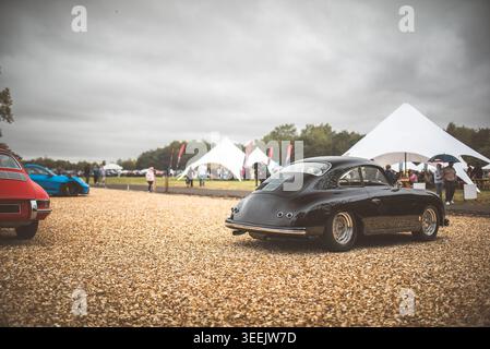 Im Mittelpunkt dieses Bildes steht ein Oldtimer-Sportwagen, der auf Schotter geparkt ist und im Hintergrund andere Fahrzeuge und Zelte stehen Stockfoto