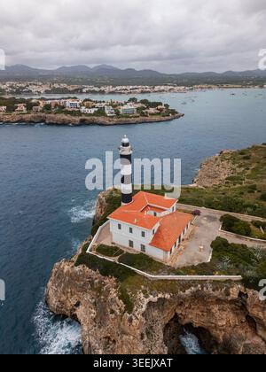 Aus der Vogelperspektive des Leuchtturms von Portocolom auf einer felsigen Klippe mit Blick auf das türkisfarbene Meer und die Küstenstadt unter einem bewölkten Himmel in Portocolom, Balearen ist Stockfoto