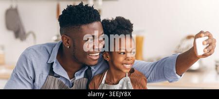 Vater und Tochter teilen sich einen Moment, während sie ein Selfie in einer hellen Küche machen Stockfoto