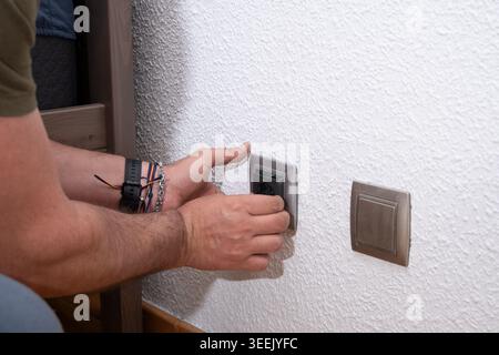 Erwachsene Hände, die ein elektrisches Bauteil an eine weiße strukturierte Wand anschließen Stockfoto
