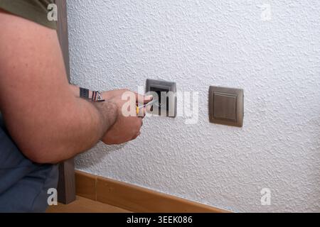 Mann, der einen Schraubendreher verwendet, um eine Steckdose an einer weißen Wand zu installieren oder zu reparieren Stockfoto