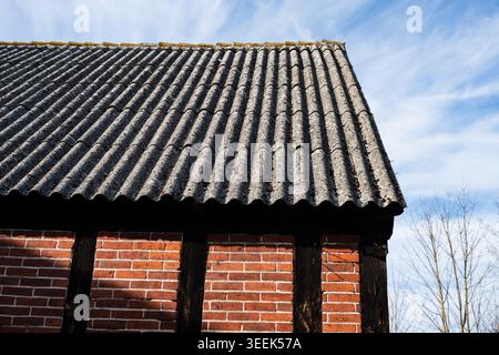 Nahaufnahme von alten, gewellten Asbestdächern, auch bekannt als eternit, auf einem alten Ziegelstein- und Holzgebäude. Stockfoto