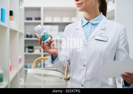 Junger Apotheker mit Ergänzungsflasche und Rezeptkontrolle in der Apotheke, Vorstellung von Medikamentenauswahl und Einzelhandelskonzept. Für Gesundheitsmarketing und Pharmazie Stockfoto
