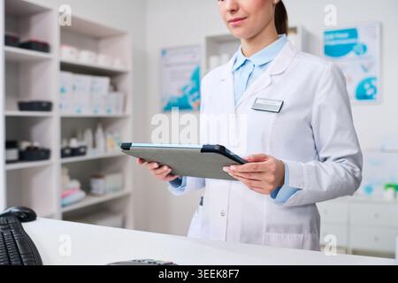 Junger Apotheker, der Tablets hält und Bestandsdaten in der Apotheke überprüft, unterstützt das Medikamentenmanagement und den Arbeitsablauf im Gesundheitswesen im Einzelhandel. Mittelgroße Aufnahme für das Pharmazie-Marketing Stockfoto