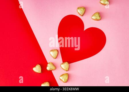 Romantische flache Lay mit rotem Papierherz und herzförmigen Pralinen auf rotem und rosa Hintergrund. Minimales Liebeskonzept. Flacher Style. Draufsicht. Stockfoto