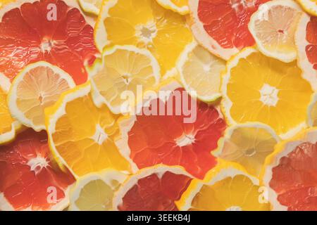 Nahaufnahme reifer saftiger Orangen-, Grapefruit- und Zitronenfruchtscheiben, mit Wasser, das von oben gewellt ist. Heller, farbenfroher und erfrischender Hintergrund für gesunde f Stockfoto