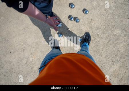 Erste Person: Blick von oben nach unten auf Stahlkugeln auf dem Sandplatz zwischen zwei Spielern, die mit Standfüßen stehen, einzigartige Sicht auf die Außenbarren Stockfoto