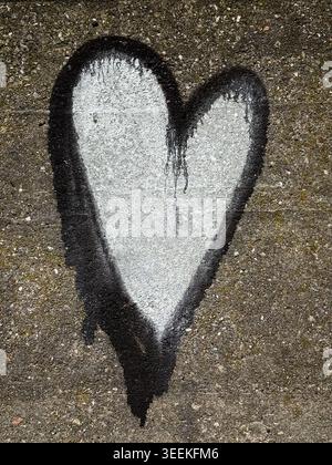 Weißes Graffiti-Herz mit schwarzer Farbe auf einer rauen Betonwand mit sichtbarer Textur und Farbtropfen. Stockfoto