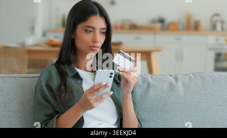 Ernsthafte indische Frau zu Hause mit Telefon machen Zahlung Kreditkarte Kreditkarte mobil Online-Shopping surfen Arabische weibliche Kundenkundenin Dame Stockfoto