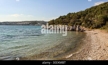Kiesstrand in Bitez Bay, Bodrum, Türkei, mit ruhigem, klarem türkisfarbenem Wasser der Ägäis und grünen Hügeln unter blauem Himmel Stockfoto