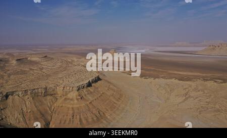 Eine weitläufige Luftperspektive zeigt zerklüftetes Wüstengelände mit dramatischen Canyonwänden und erodierten Sedimentschichten unter einem weiten offenen Himmel. Stockfoto