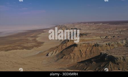 Eine weitläufige Luftperspektive zeigt dramatische Wüstenschluchten, die in erdfarbene Sedimentschichten unter einem ruhigen blauen Himmel mit minimalem Clou gehauen sind Stockfoto