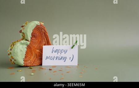 HAPPY MORNING Saying Card köstliches frisches Croissant mit Matcha Green Tea Flavor Ganache. Creation einzigartige Bäckerei in Herzform. Blätterteig Urlaub Liebe Geschenk Geschenk Idee Valentinstag. Kopierbereich Stockfoto