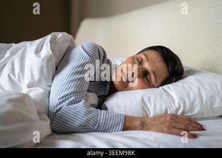 Ruhige ältere Frau, die bequem im Bett lag und mit einer gemütlichen Decke bedeckt war. Stockfoto
