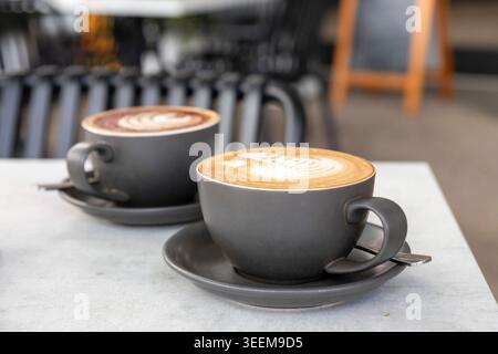 Zwei Tassen frischer Kaffeespezialitäten mit professioneller Latte Art serviert an einem modernen Tisch im Freien in einem lokalen Café in Brisbane, Queensland, Australien. (2 Stockfoto