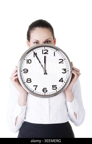 Geschäftsfrau, die eine Uhr vor dem Gesicht hält. Isoliert auf weiß Stockfoto