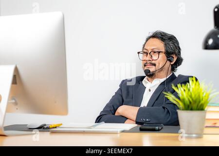 Ein junger männlicher Mitarbeiter kommuniziert mit Kollegen über ein virtuelles Meeting auf seinem Laptop in einer modernen Büroumgebung. Stockfoto