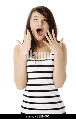Überraschte junge Frau, die vor Aufregung schreiend und Hände und Finger zeigt. Langhaarige Brünette mit Augen nach oben und offenem Mund, gestreift, b Stockfoto