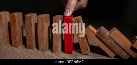 Versicherung mit Händen schützt Domino. Geschäftsmanns Hände verhindern, dass Dominosteine in die Hauskrise fallen. Kontrolle und Planung von Geschäftsrisiken sowie Strategien für die Durchführung Stockfoto