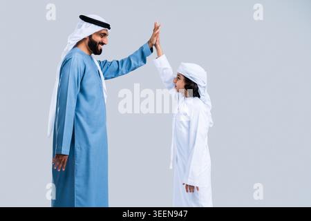 Arabischer Vater und Sohn. Gekleidet in traditionellen emirat Kandoras und Kopfbedeckungen. Sind High Fiving vor Freude und Lächeln. Darstellung von Familienverbänden. Erfolgreich p Stockfoto