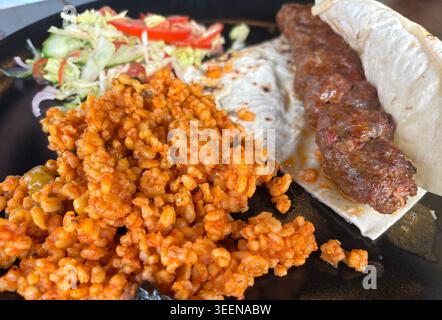 Türkischer Hühnchenkebab mit Bulgur, Salat und Lavash aus nächster Nähe. Gegrilltes Hackfleisch mit Gewürzen auf verschwommenem Hintergrund Stockfoto