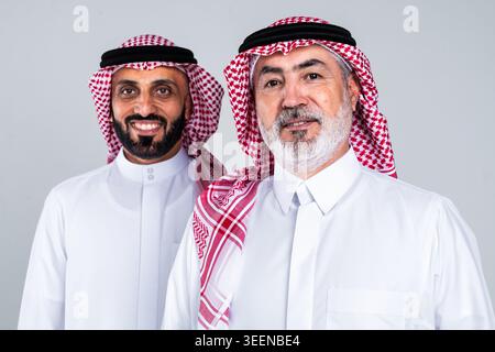 Zwei saudi-arabische Männer, Vater und Sohn, stehen zusammen und blicken in die Kamera, zeigen einen fröhlichen Ausdruck und verkörpern traditionelle mittlere eas Stockfoto